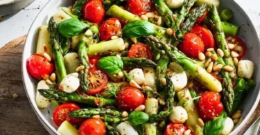 Grüner Spargel Salat mit Tomaten und Mozzarella auf einem weißen Teller.